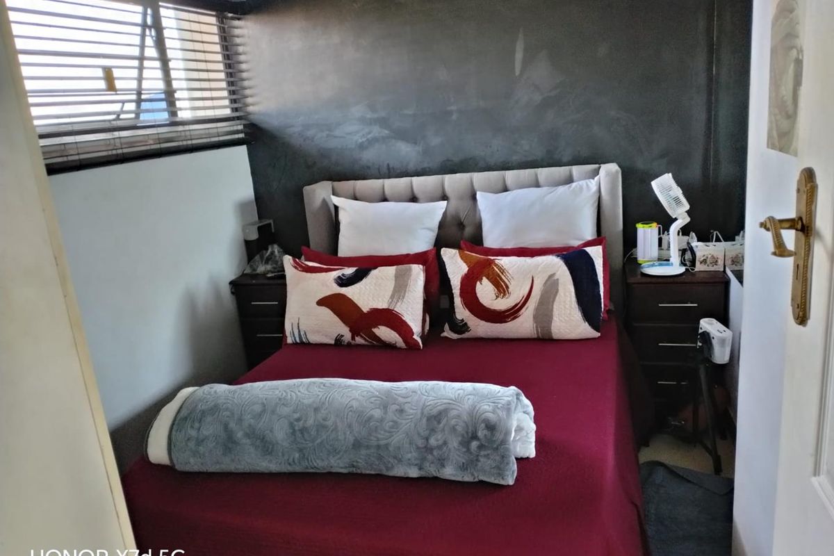 A compact bedroom featuring a dark accent wall, horizontal window blinds, and neutral flooring, providing a cozy and functional sleeping space.