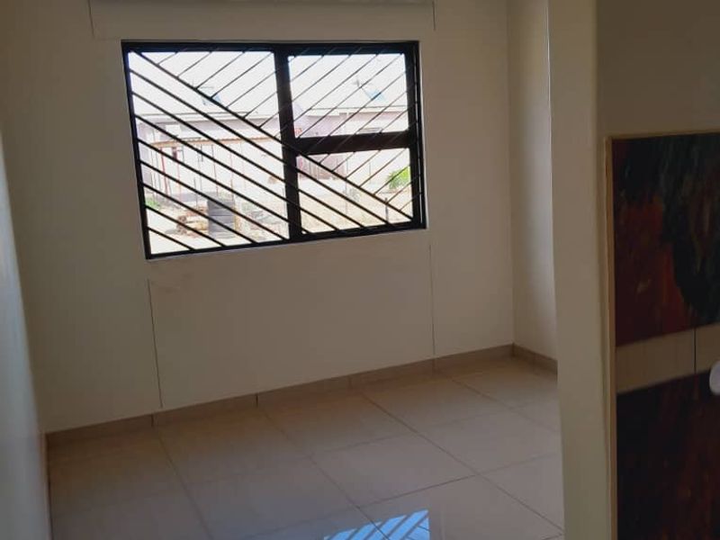 A clean, empty bedroom featuring neutral tiled flooring, a window with security bars, and a simple ceiling light fixture.