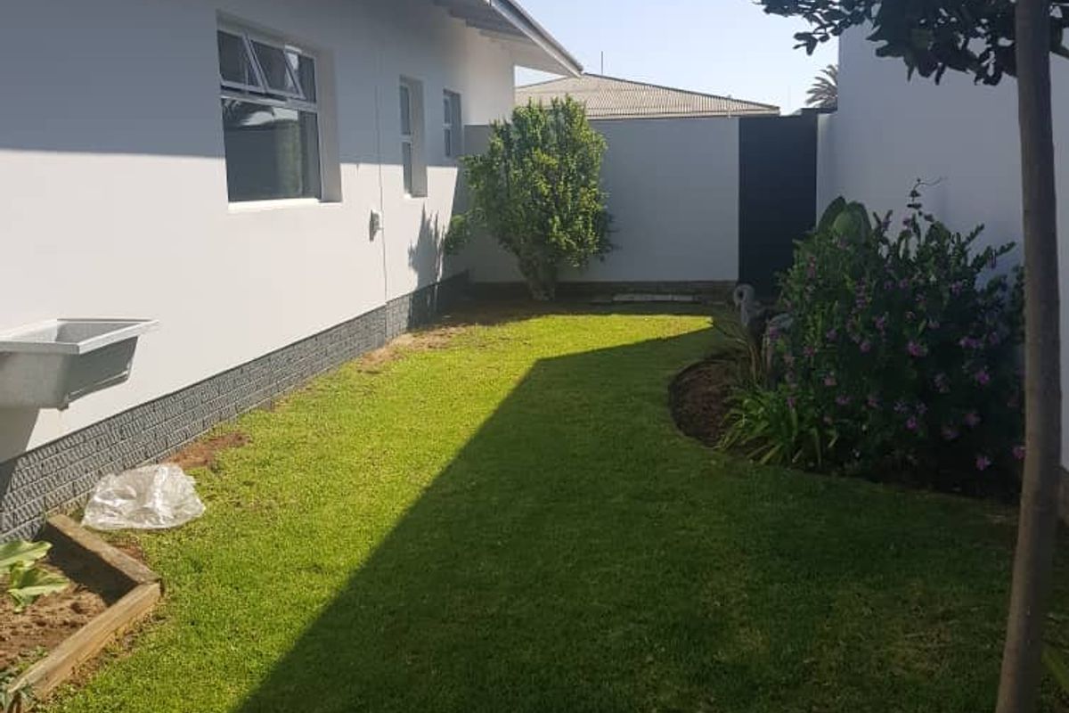 A side garden area featuring a lawn, perimeter wall, and an exterior utility sink mounted to the house wall.