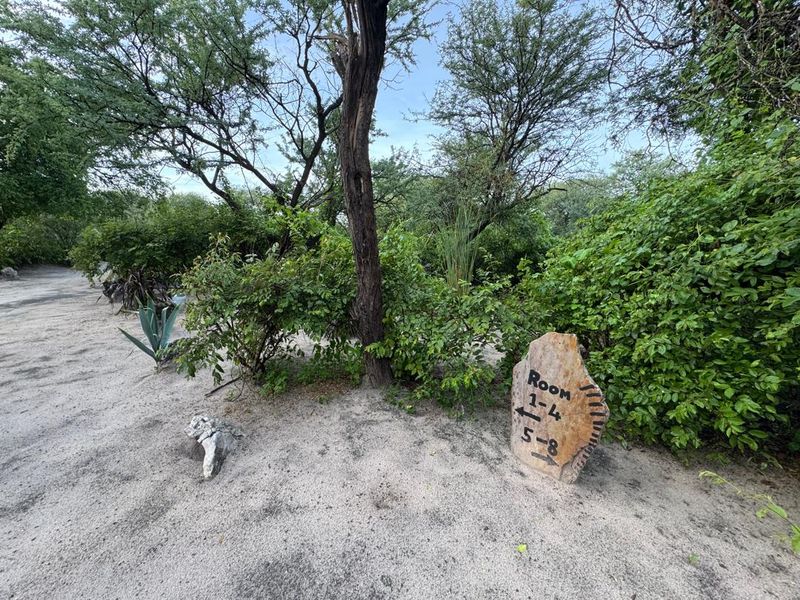 A natural garden setting featuring a sandy pathway and directional signage for guest accommodation units.