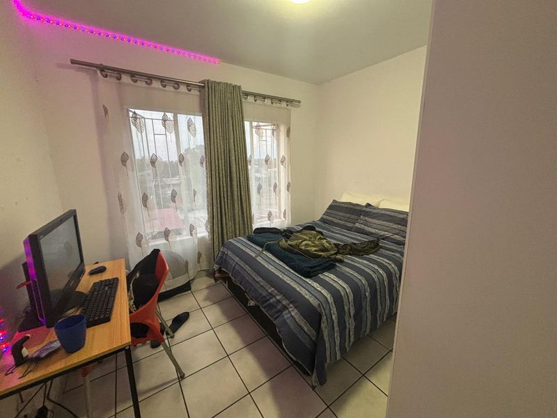 A functional bedroom featuring tiled flooring and windows fitted with security bars, providing a practical living space.