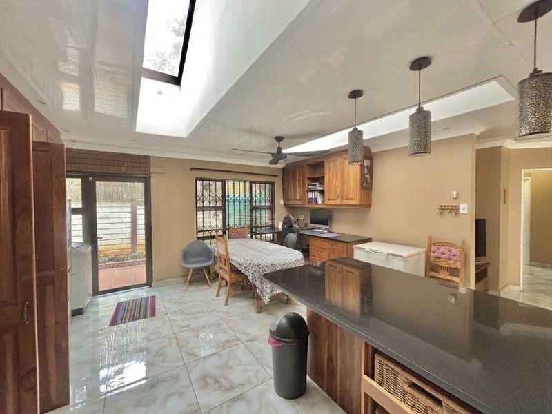 Spacious open-plan living and kitchen area featuring a large skylight, tiled flooring, built-in wooden cabinetry, and a stone-topped kitchen island.