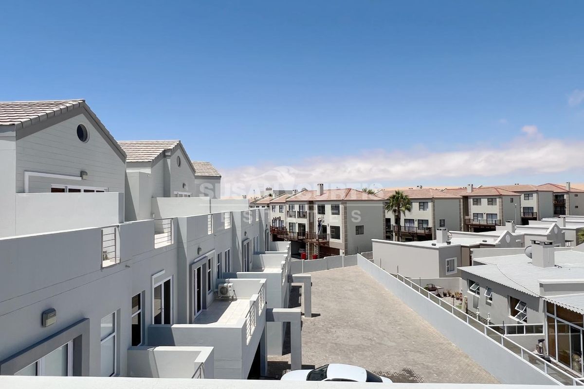 Elevated view of a modern townhouse complex featuring paved driveways, balconies, and tiled roofing under a clear sky.