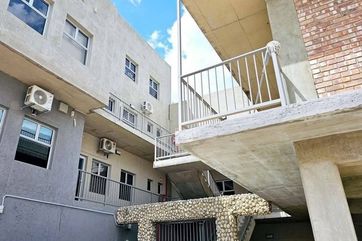Exterior view of a multi-story office building featuring concrete balconies, metal railings, and wall-mounted air conditioning units.