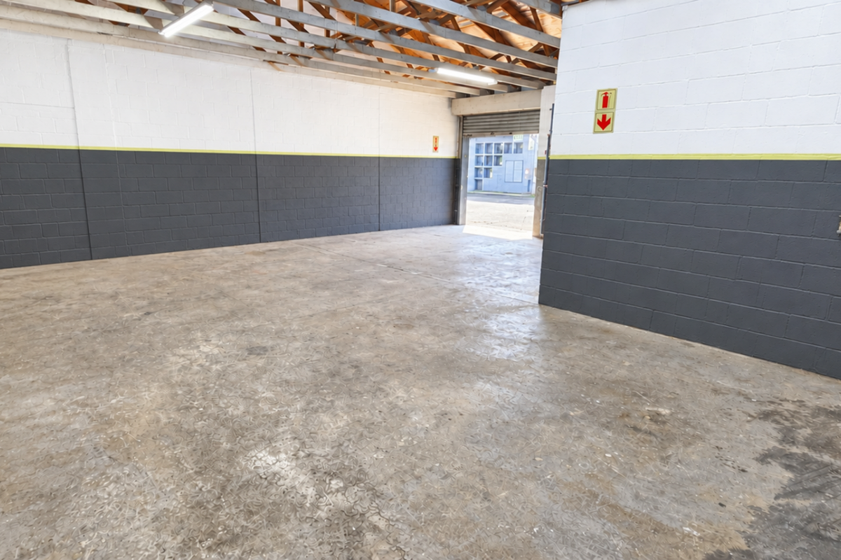 Spacious industrial garage featuring exposed timber roof trusses, durable concrete flooring, and painted block walls with a roller shutter door entrance.