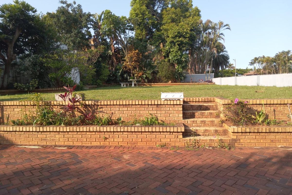 A spacious rear garden featuring tiered face-brick retaining walls, brick-paved patio area, and established lawn with mature trees.