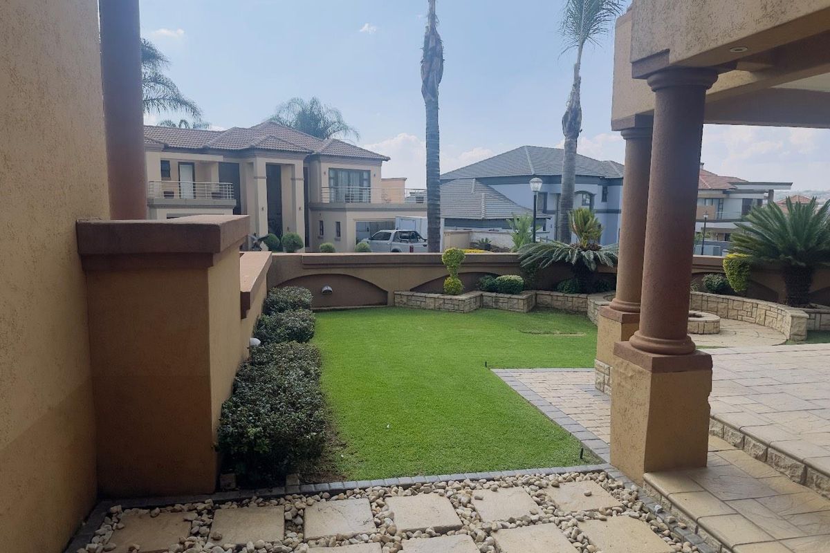 A well-maintained rear garden featuring a manicured lawn, paved patio area, stone retaining walls, and established landscaping.