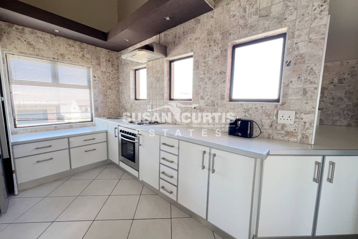 A functional kitchen featuring white cabinetry, stone-tiled splashbacks, built-in oven, extractor fan, and tiled flooring with ample natural light.
