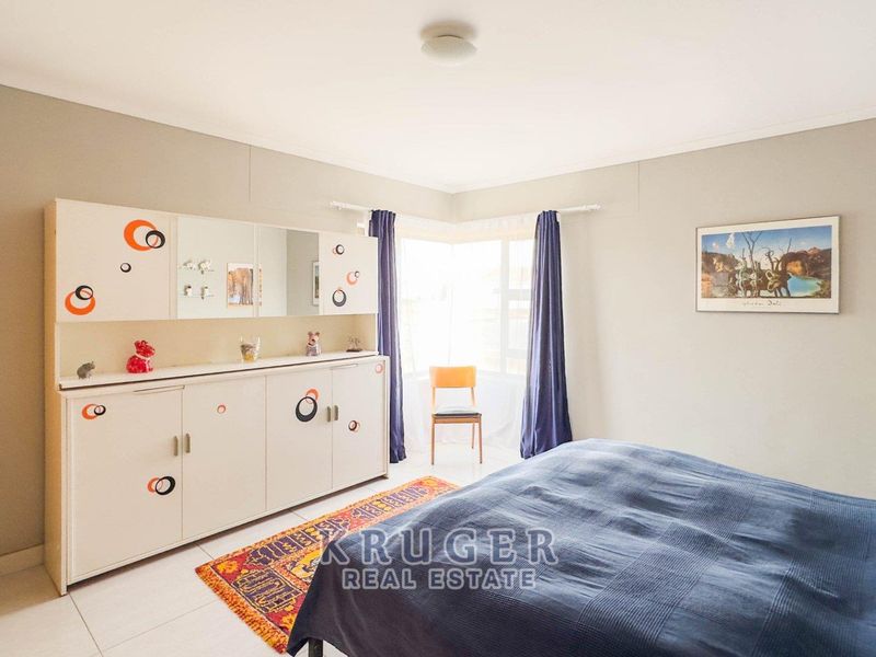 A bedroom featuring tiled flooring, built-in cupboards, and a corner window allowing natural light.