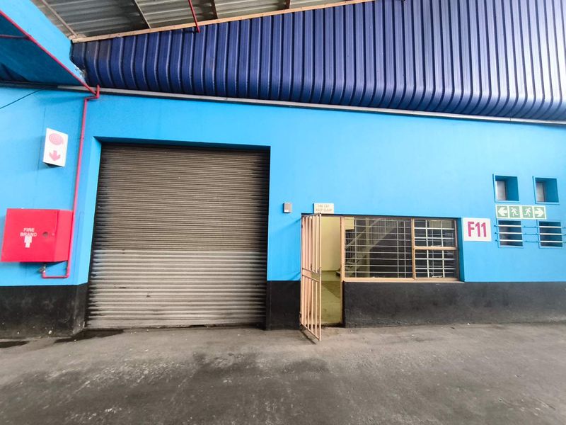 Industrial utility space featuring a large roller shutter door, security gate, fire safety equipment, and high-clearance corrugated metal roofing.