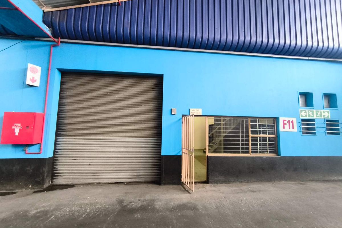 Industrial utility space featuring a large roller shutter door, security gate, fire safety equipment, and high-clearance corrugated metal roofing.