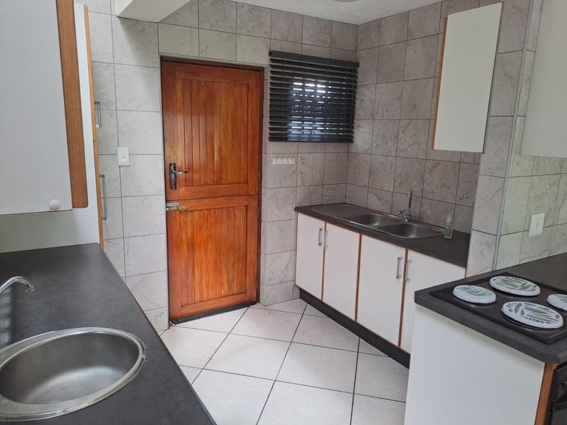 A functional kitchen featuring dual sink areas, laminate countertops, tiled finishes, and built-in cabinetry with direct access to an exterior timber door.