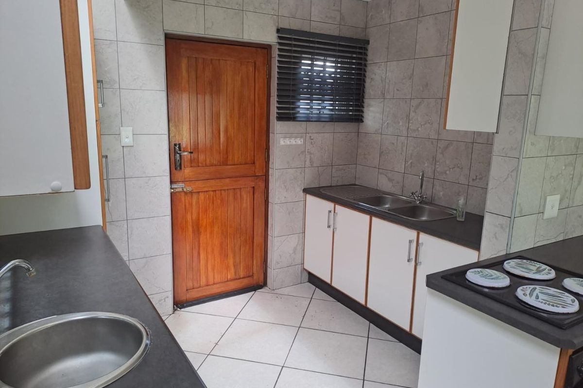 A functional kitchen featuring dual sink areas, laminate countertops, tiled finishes, and built-in cabinetry with direct access to an exterior timber door.