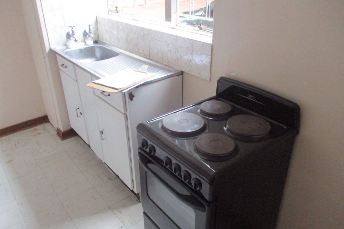 A compact kitchen featuring a stainless steel sink, basic white cabinetry, and a freestanding electric stove with solid plates.