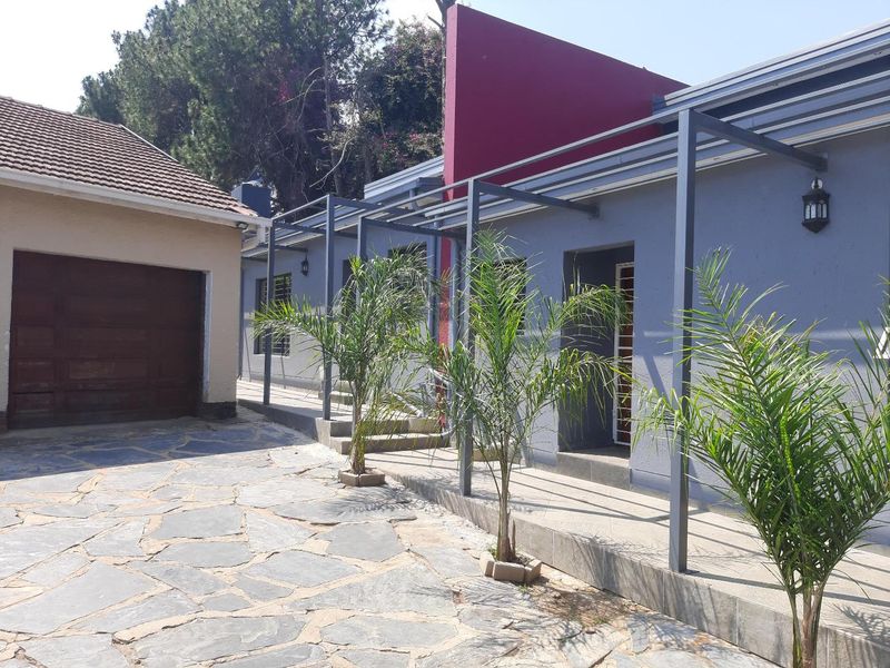 Front exterior view of the cottage featuring a paved driveway, attached garage, and a covered walkway with a modern metal pergola structure.
