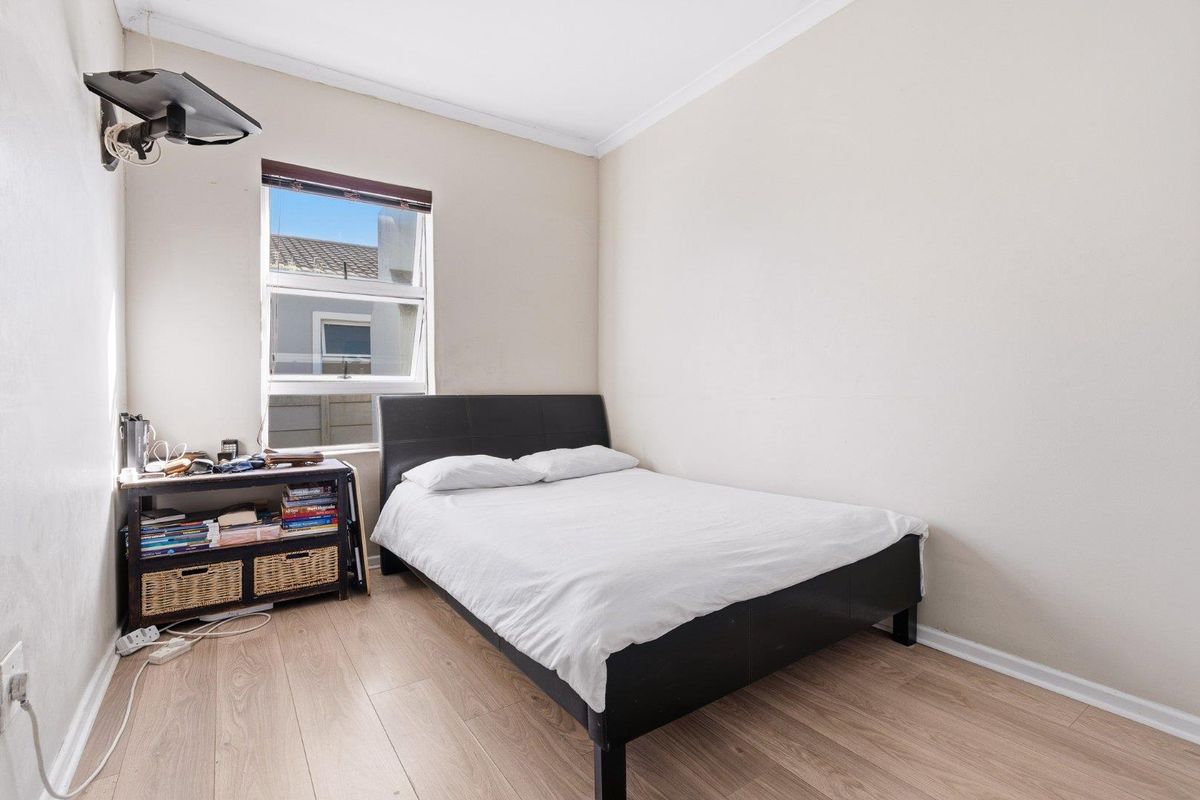 A functional bedroom featuring light-toned laminate flooring, neutral wall finishes, and a window providing natural light.