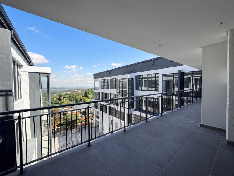 A spacious, modern covered balcony featuring sleek tiled flooring, a secure metal balustrade, and recessed lighting, offering expansive views of the surrounding area.