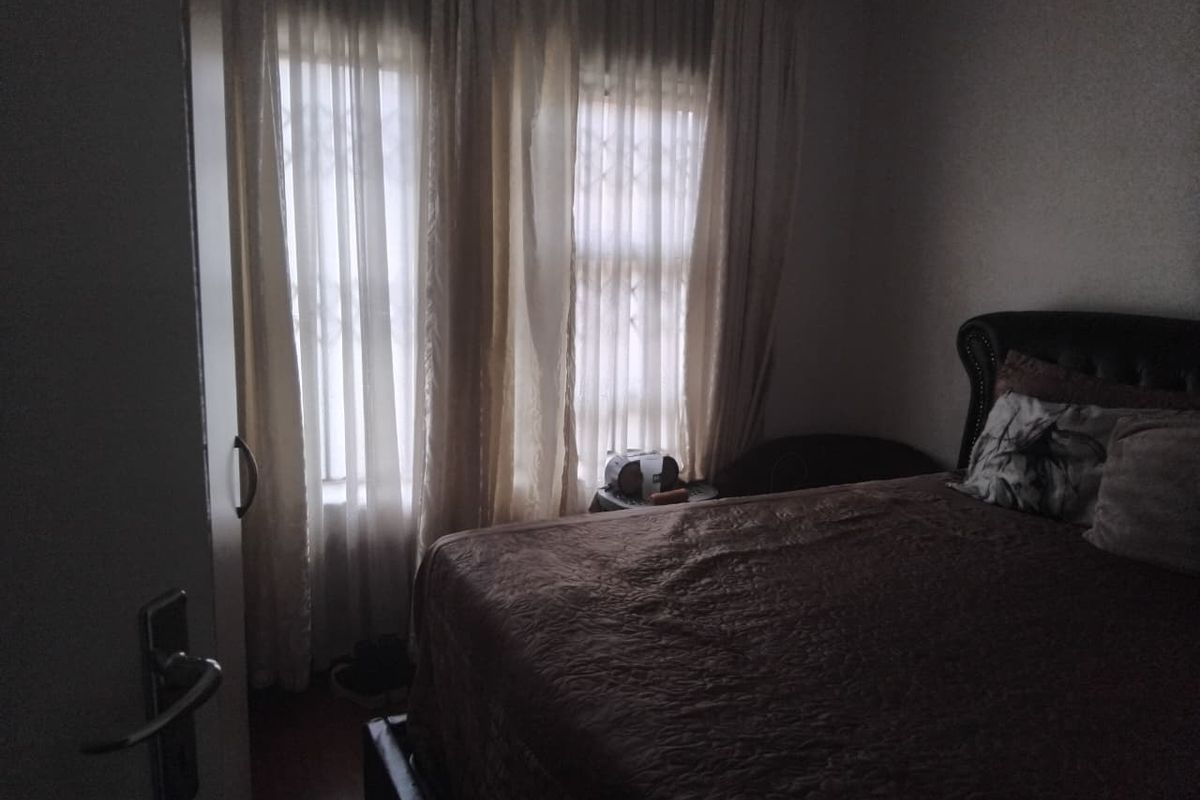 A bedroom featuring laminate flooring and windows fitted with security bars, currently dimly lit.