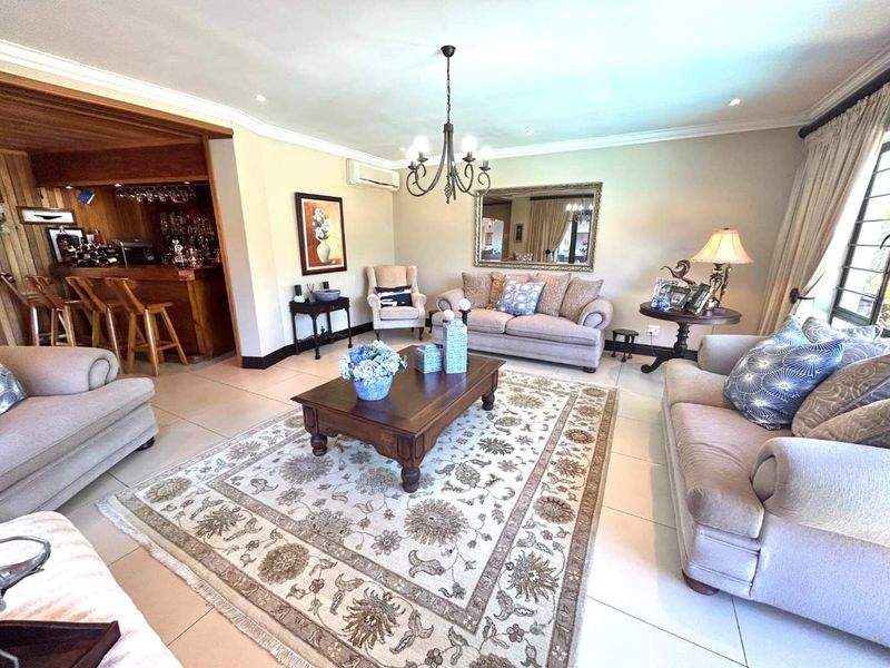 Spacious open-plan living area featuring tiled floors, a built-in bar, split-system air conditioning, and elegant crown molding throughout.