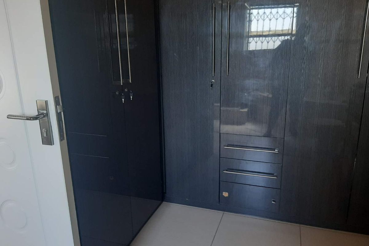 A bedroom featuring modern, dark-toned built-in cupboards with integrated drawers and sleek metal handles, complemented by neutral floor tiling.