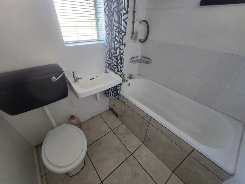 A compact bathroom featuring a bathtub, wall-mounted basin, and high-level cistern toilet, with tiled flooring and splashback areas.