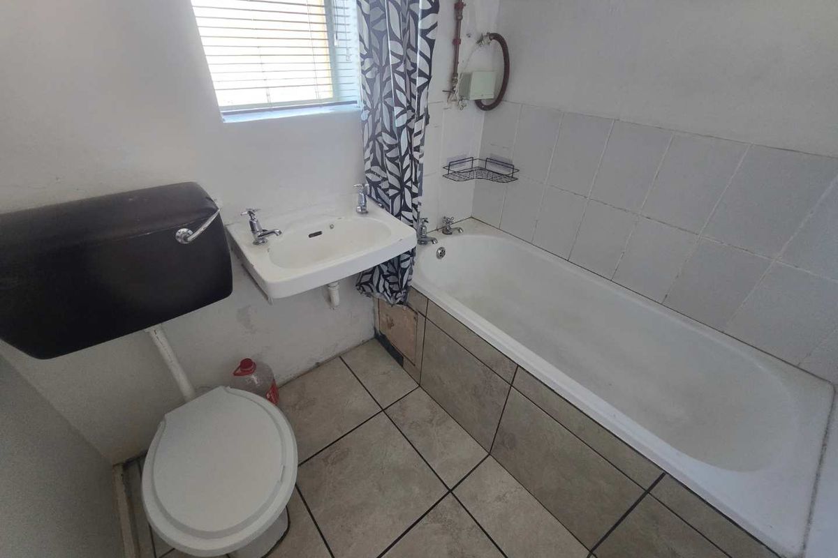 A compact bathroom featuring a bathtub, wall-mounted basin, and high-level cistern toilet, with tiled flooring and splashback areas.