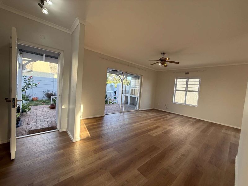Spacious, light-filled living room featuring modern laminate flooring, a ceiling fan, and direct access to an outdoor patio area through sliding glass doors.