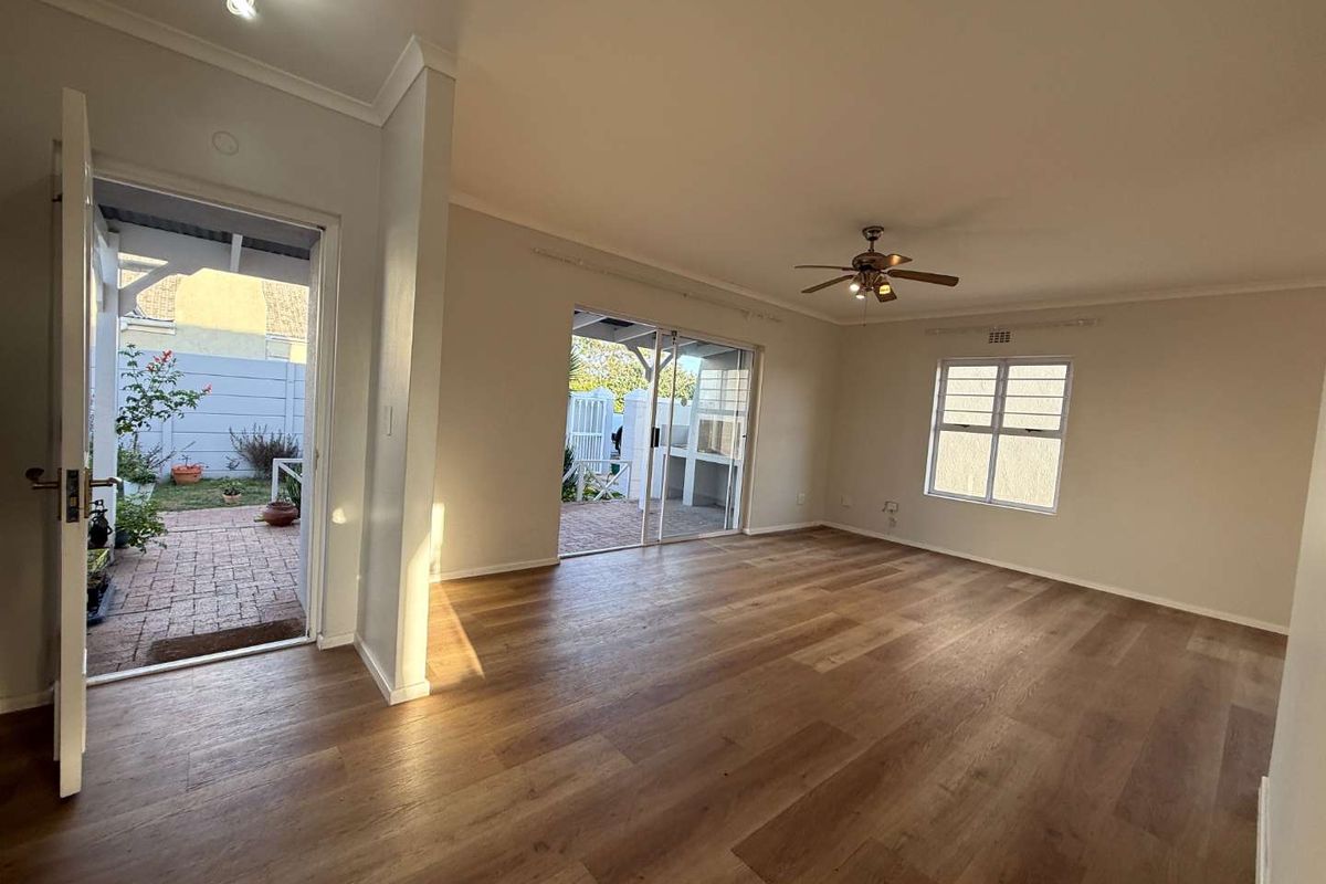 Spacious, light-filled living room featuring modern laminate flooring, a ceiling fan, and direct access to an outdoor patio area through sliding glass doors.