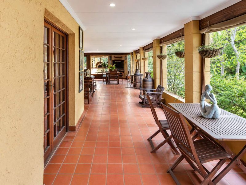 Spacious covered patio featuring terracotta tiling, recessed lighting, and timber-framed glass doors, offering a seamless transition to the garden area.
