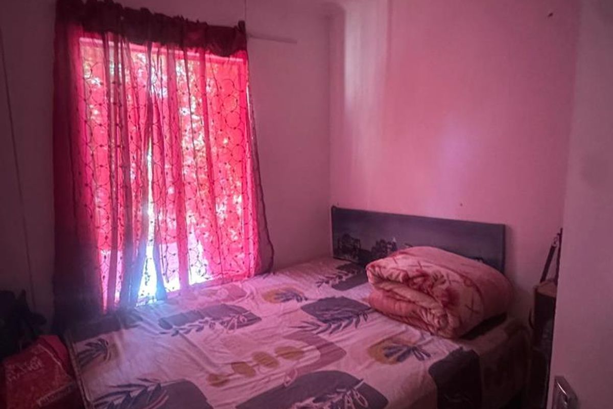 A compact bedroom featuring a window with red curtains and basic interior finishes, suitable for a small guest room or study.