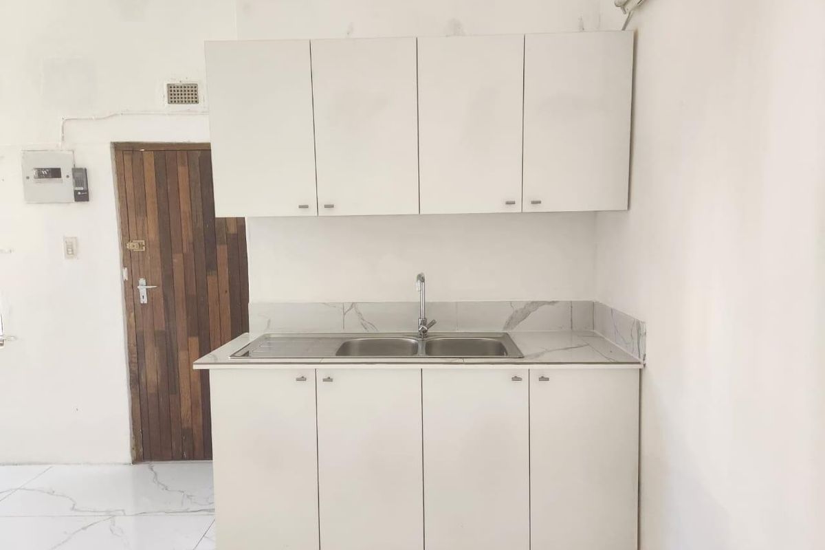A compact kitchen area featuring white built-in cabinetry, a stainless steel double sink, and marble-look countertops with matching backsplash.