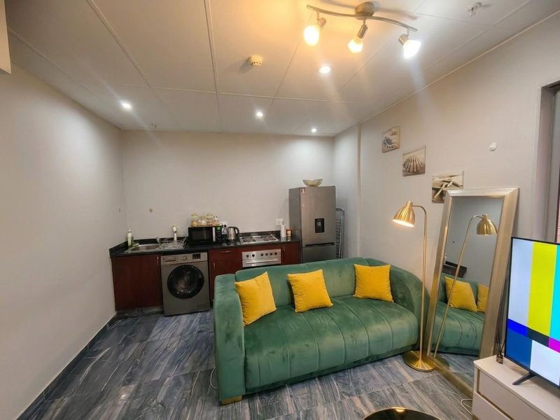 Compact open-plan living area featuring a kitchenette with built-in cabinetry, oven, hob, and integrated sink, finished with modern tiled flooring.