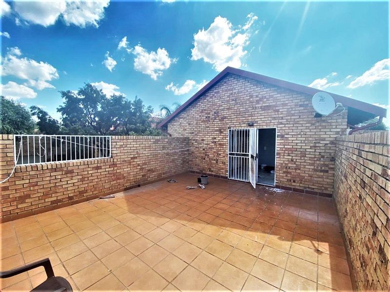 An open-air paved patio area enclosed by brick boundary walls, featuring a security gate entrance and a satellite dish mounted on the exterior wall.