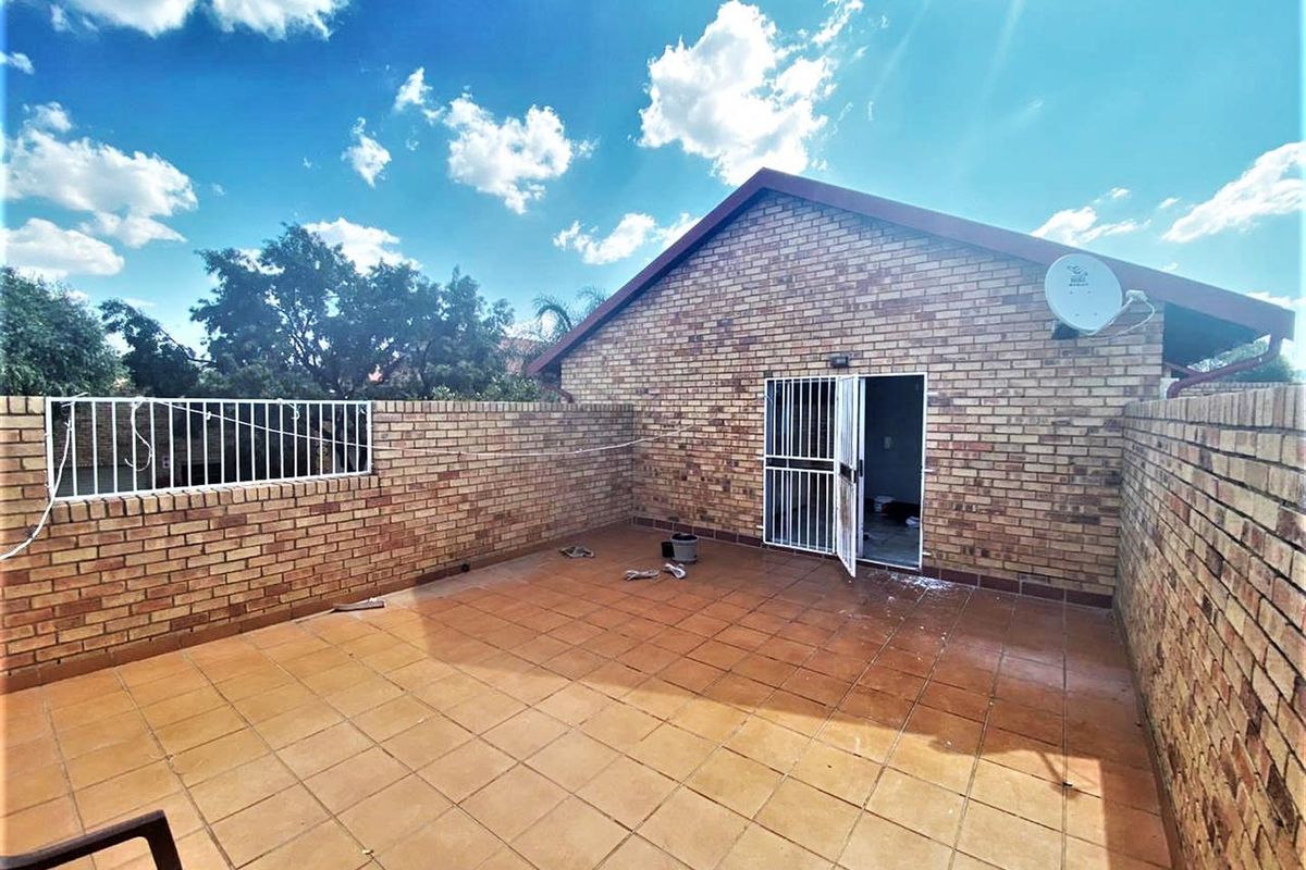 An open-air paved patio area enclosed by brick boundary walls, featuring a security gate entrance and a satellite dish mounted on the exterior wall.