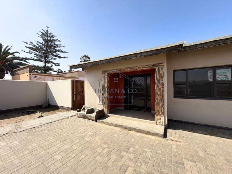 Front exterior view of the property featuring a paved driveway, stone-clad entrance, and secure boundary walling.