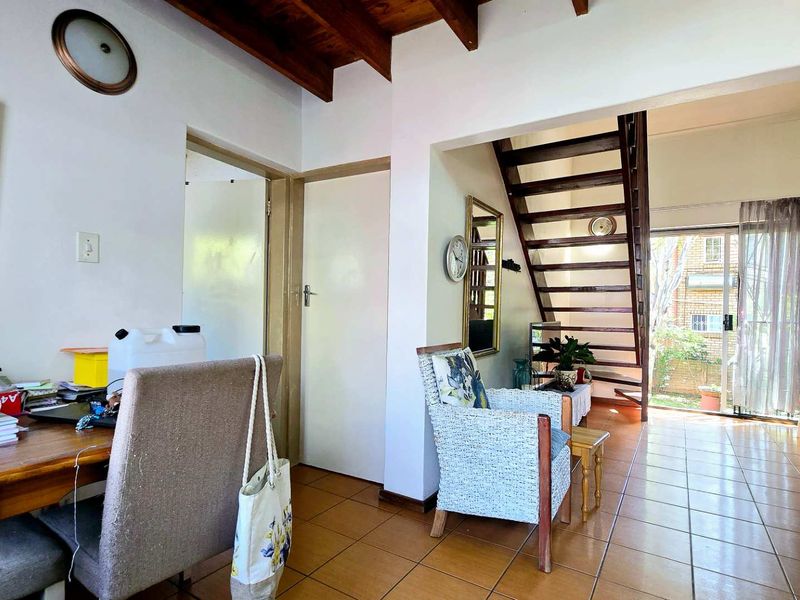 Living area featuring exposed timber ceiling beams, ceramic floor tiles, and a timber staircase leading to the upper level with access to the rear garden.
