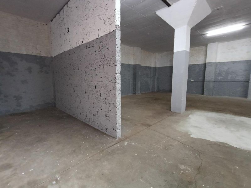 An open-plan industrial utility space featuring concrete flooring, structural columns, and painted masonry walls, suitable for storage or workshop use.