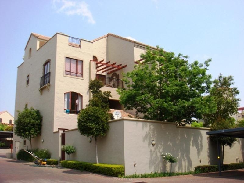 A multi-story apartment building featuring a stucco facade, timber pergola, and private balconies with wrought iron railings, set within a well-maintained complex.