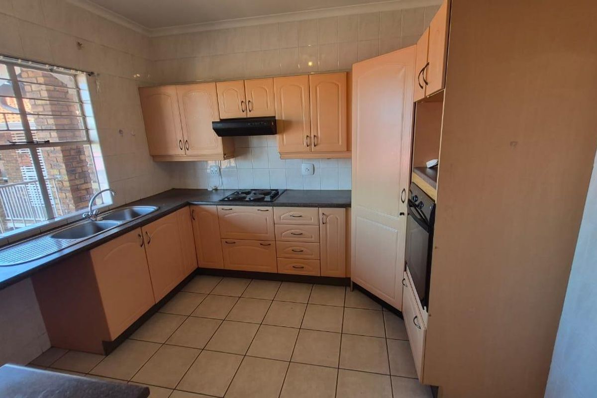 A functional kitchen featuring light-toned cabinetry, a built-in oven, hob, extractor fan, and a double-basin sink with tiled splashbacks.
