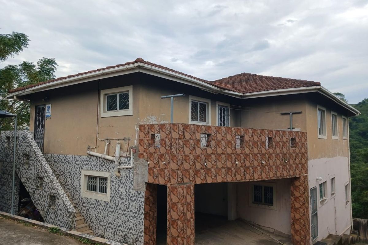 Rear view of a multi-level house featuring a tiled roof, external staircase, and a covered parking area with visible exterior wear.