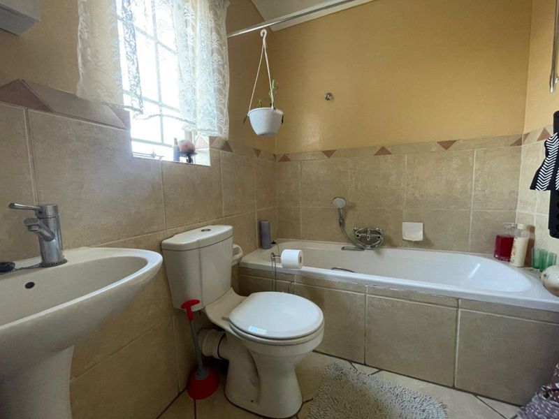 A functional bathroom featuring a pedestal basin, toilet, and a bathtub with a shower mixer, finished with neutral wall and floor tiling.