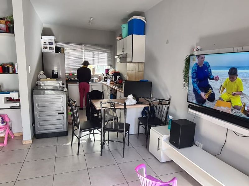 Open-plan living and kitchen area featuring tiled flooring, built-in shelving, and a wall-mounted television unit.
