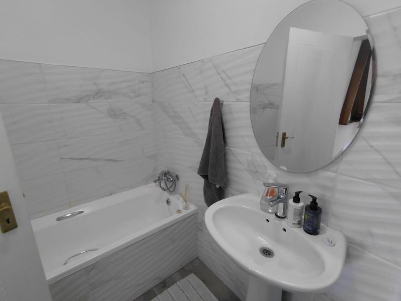 A clean, modern bathroom featuring white marble-effect wall tiles, a pedestal basin, and a bathtub with chrome fixtures.
