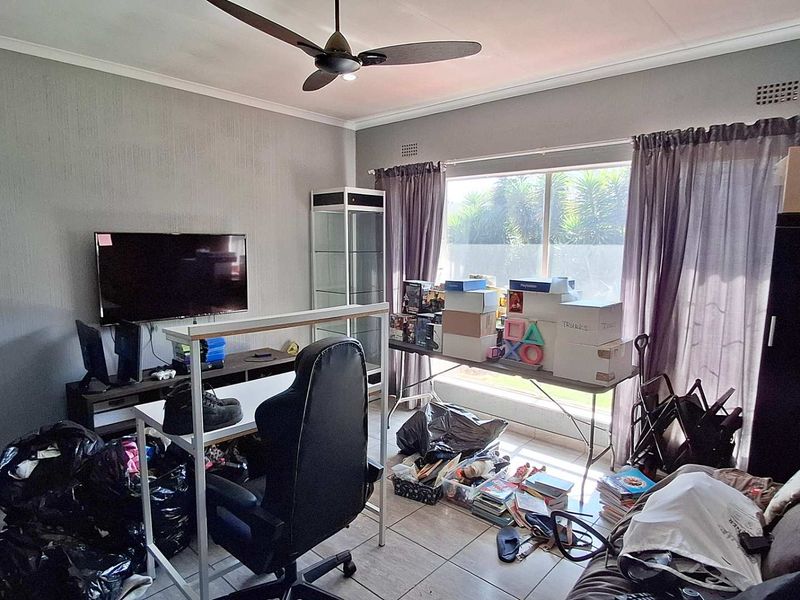 A living room featuring tiled flooring, a ceiling fan, and a large window providing natural light.