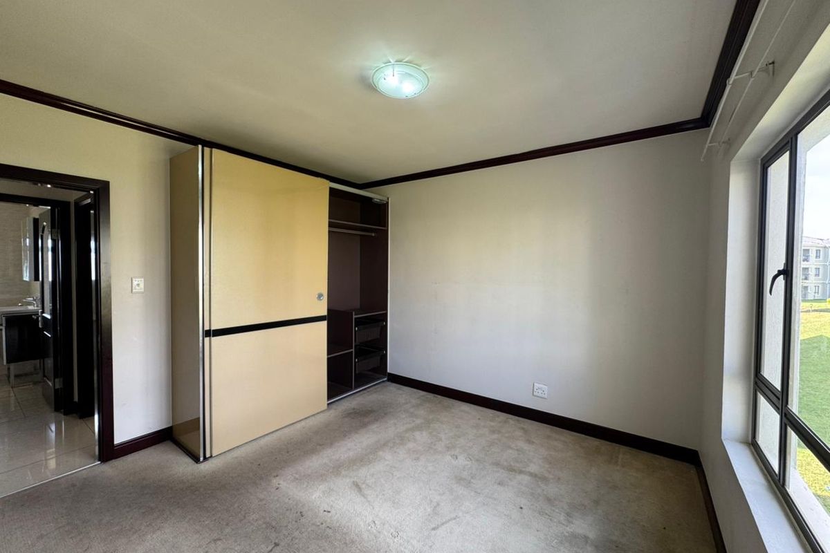 A bedroom featuring built-in sliding door wardrobes, carpeted flooring, and large windows providing natural light, with an adjacent bathroom visible.