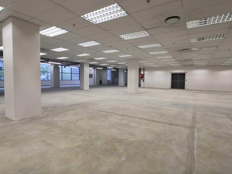 A large, open-plan retail or office space featuring concrete flooring, suspended ceilings with recessed lighting, and structural columns.