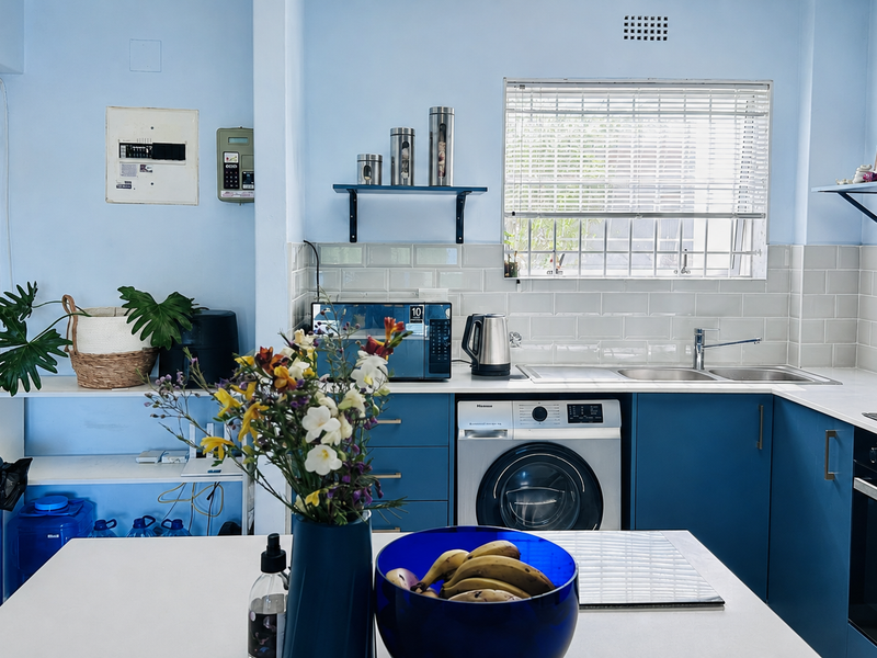A functional kitchen featuring blue cabinetry, subway tile backsplash, built-in oven, hob, and an integrated washing machine under the counter.