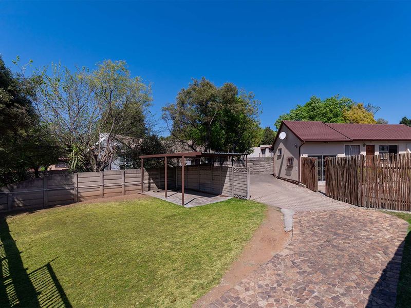 Rear exterior view featuring a paved driveway, a small covered patio structure, a lawn area, and secure boundary walling.