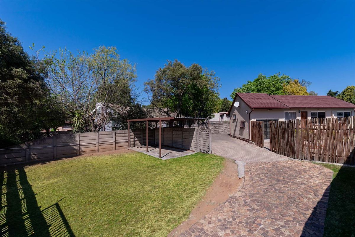 Rear exterior view featuring a paved driveway, a small covered patio structure, a lawn area, and secure boundary walling.