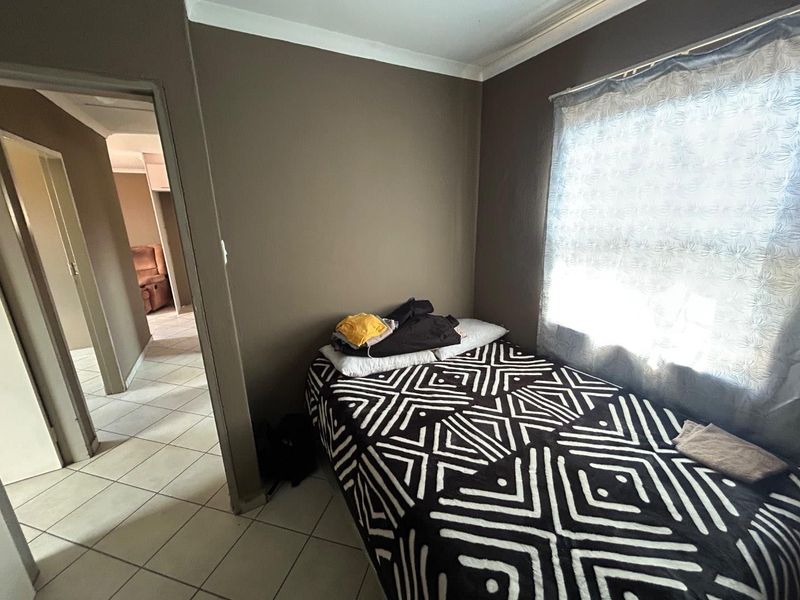 A bedroom featuring tiled flooring and neutral wall tones, with a view leading into the adjacent hallway.